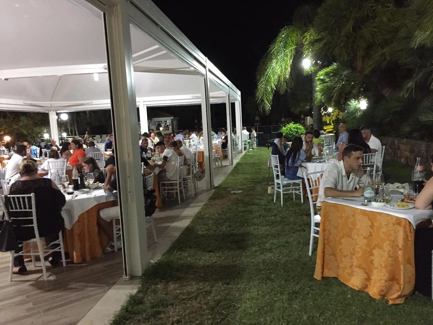 Cena all'aperto sotto tensostruttura con tavoli apparecchiati e ospiti