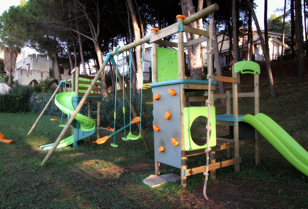 Area giochi per bambini con scivoli colorati e altalene nel giardino tra i pini
