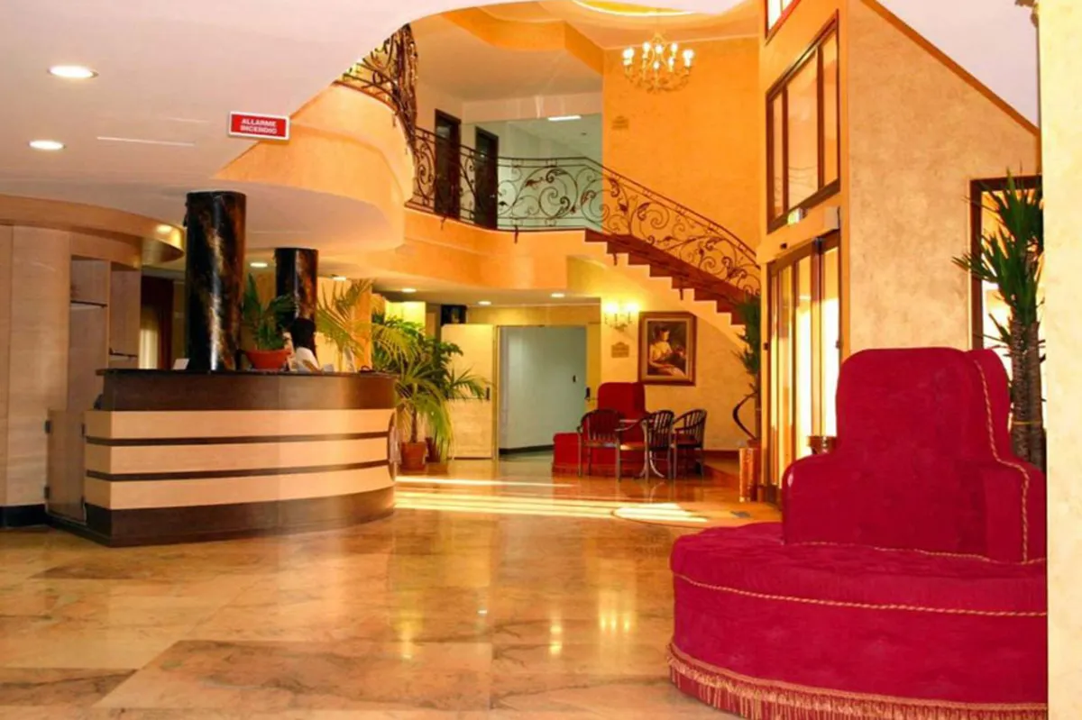 Hall dell'hotel con reception, scala elegante e poltrone rosse su pavimento in marmo