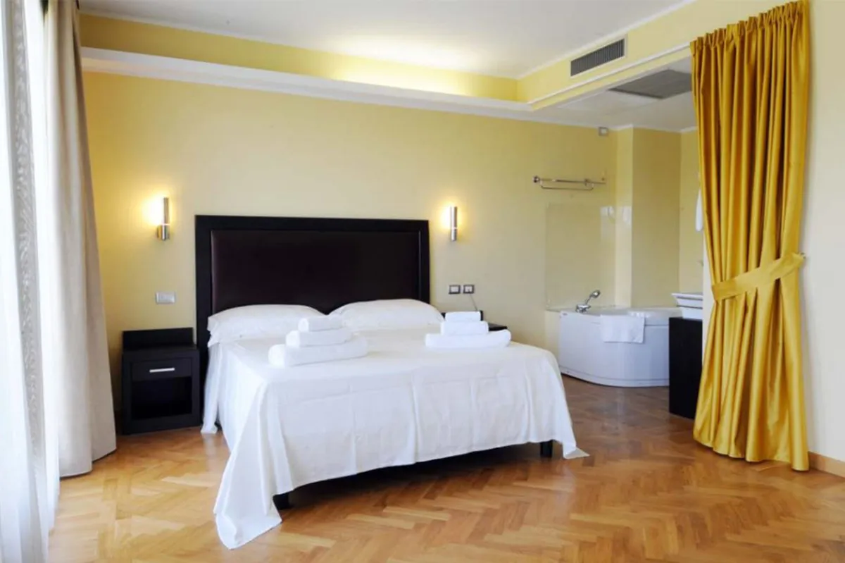 Camera matrimoniale con pareti gialle, letto bianco e vasca idromassaggio