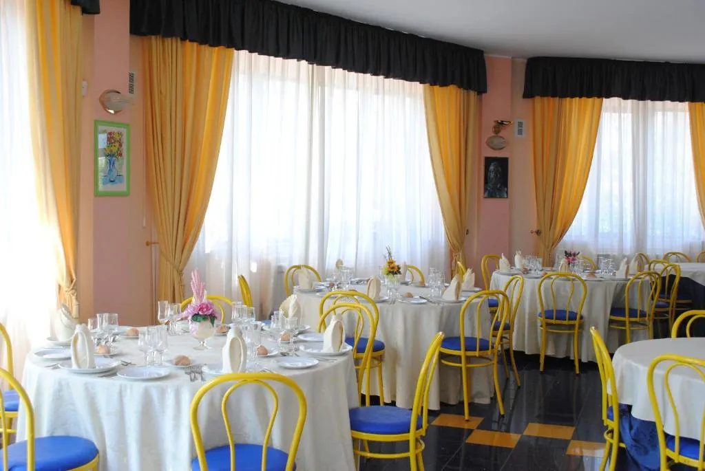 Sala ristorante con tavoli rotondi apparecchiati, tende gialle e sedie blu