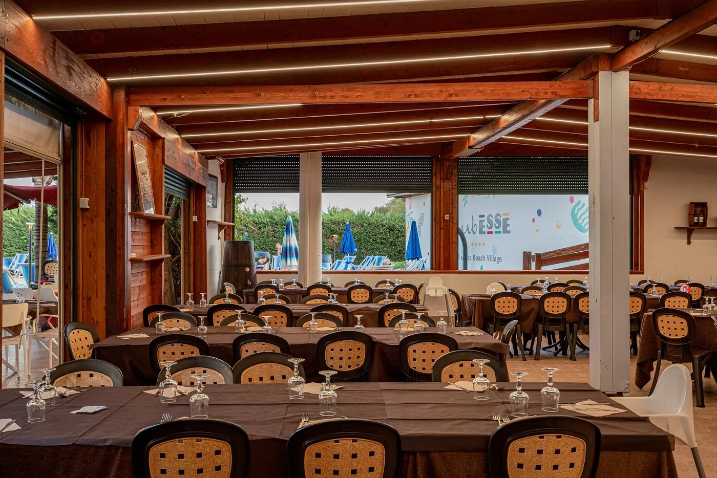 Sala ristorante con travi in legno, tavoli e affaccio sulla piscina