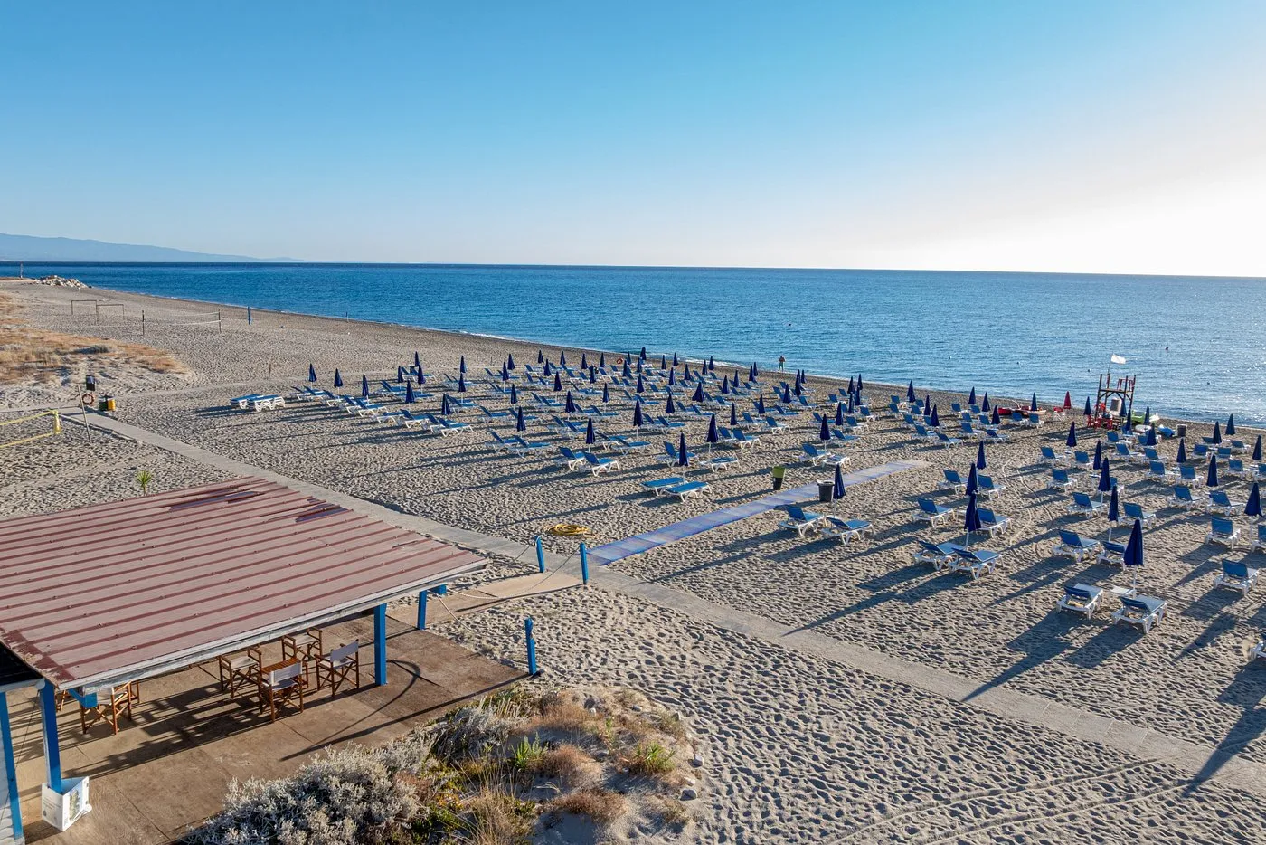 Spiaggia con file di lettini e ombrelloni chiusi e mare blu all'orizzonte