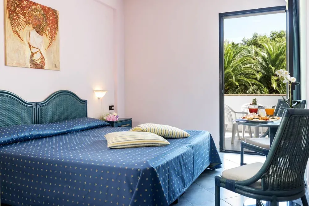 Camera con letto matrimoniale, copriletto blu e accesso al balcone sul verde