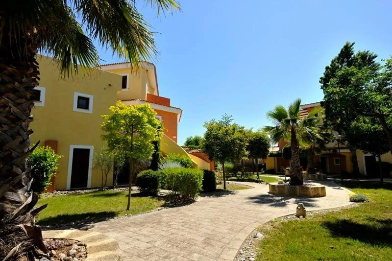 Vialetto in pietra tra edifici gialli, giardini curati e palme del resort