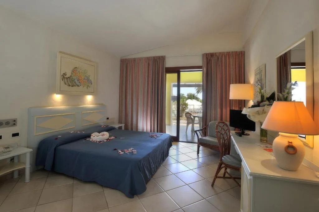 Camera da letto luminosa con copriletto blu, scrivania e uscita sulla terrazza vista giardino