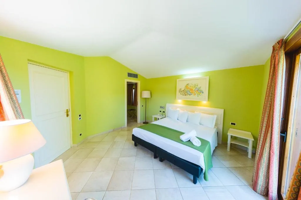 Camera da letto con pareti verdi, letto matrimoniale con asciugamani e pavimento in piastrelle chiare