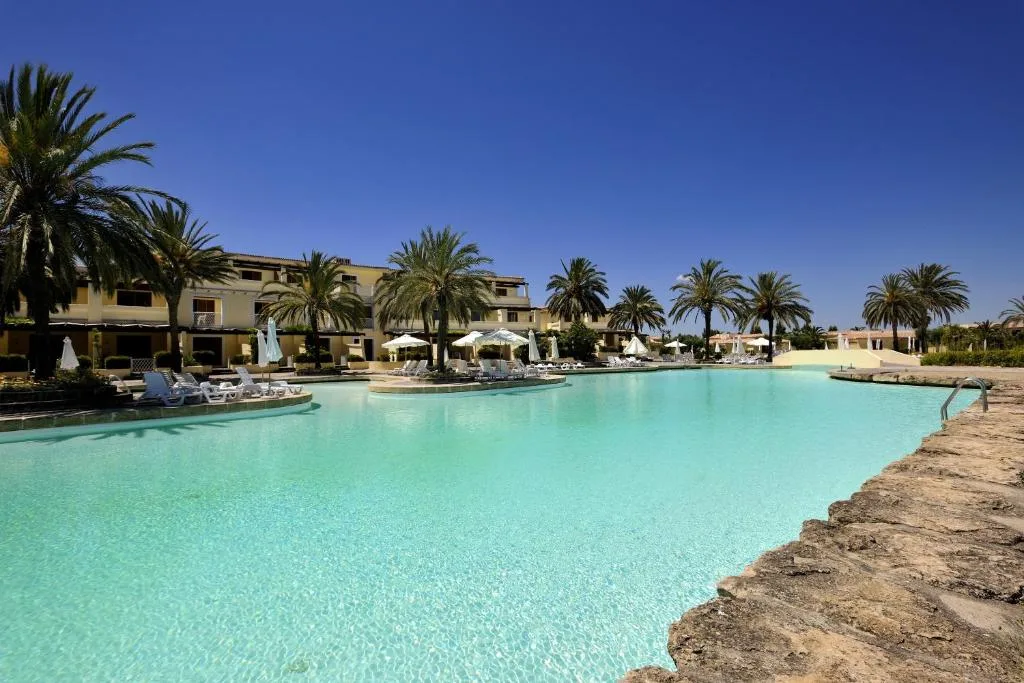 Ampia piscina turchese circondata da palme, ombrelloni ed edifici del resort