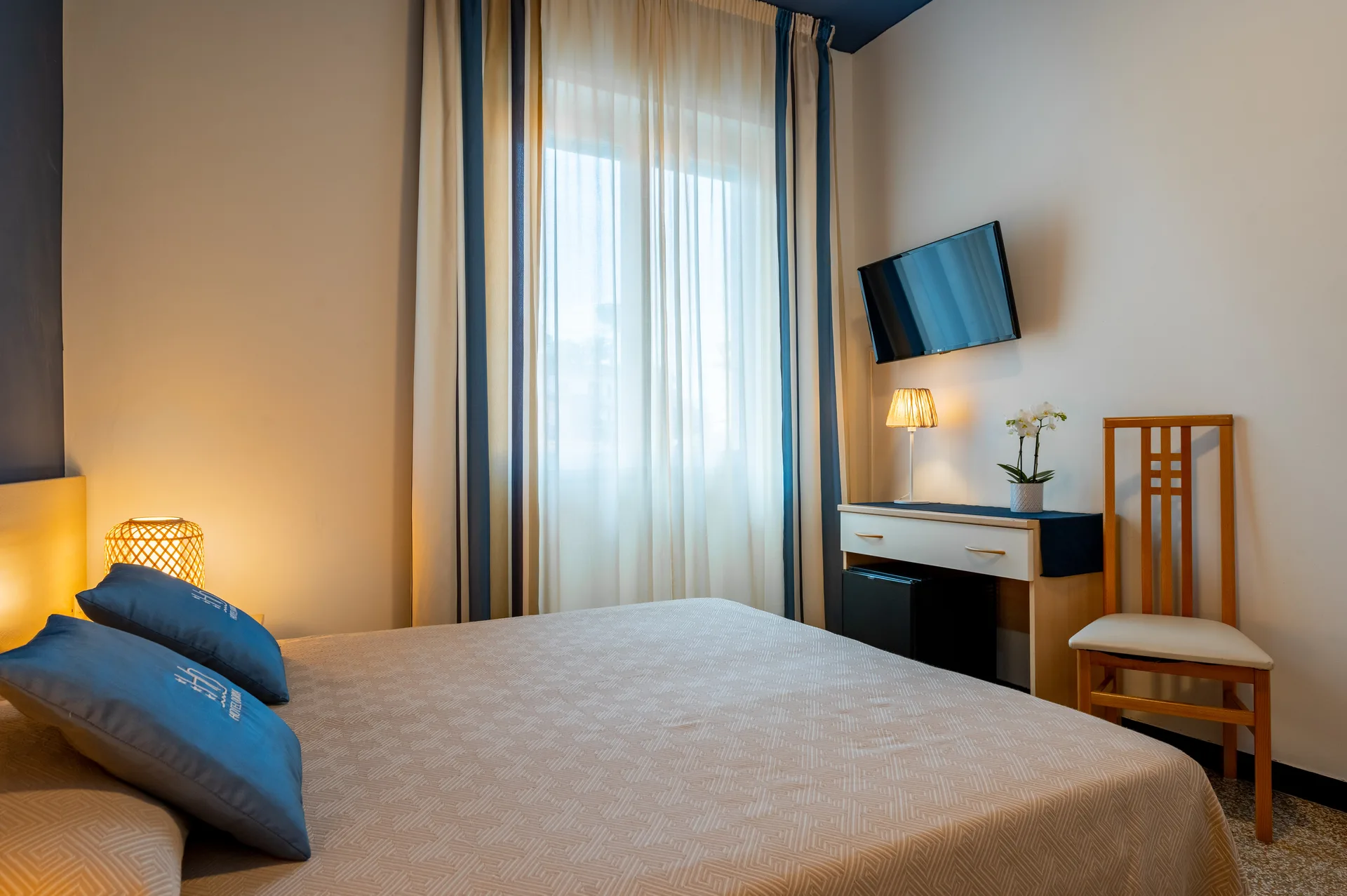 Camera da letto matrimoniale con TV a parete, scrivania e tende chiare
