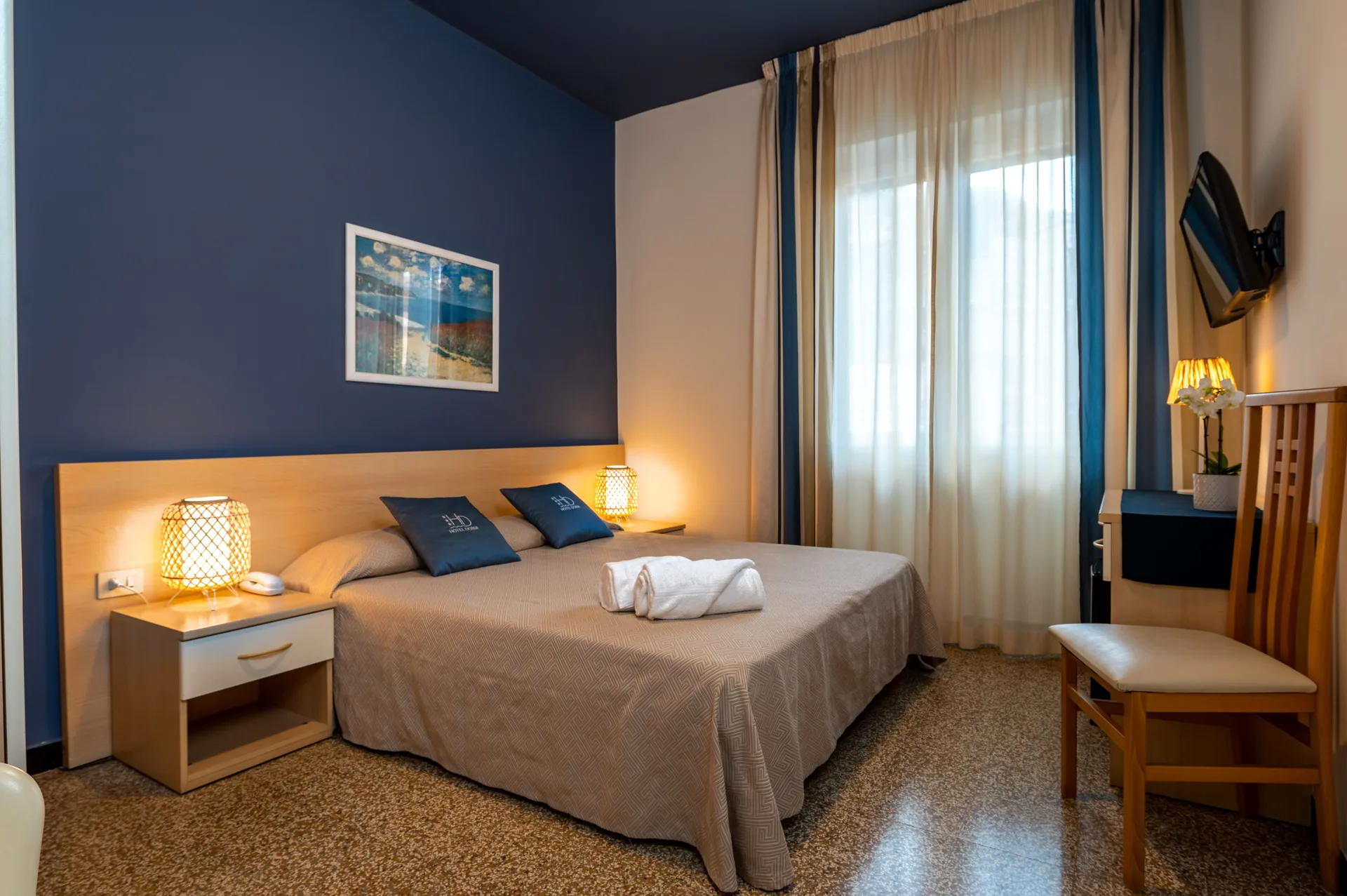 Camera matrimoniale con parete blu, quadro paesaggistico e ampia finestra luminosa