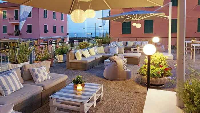Terrazza esterna con divani in rattan, cuscini e illuminazione soffusa al tramonto