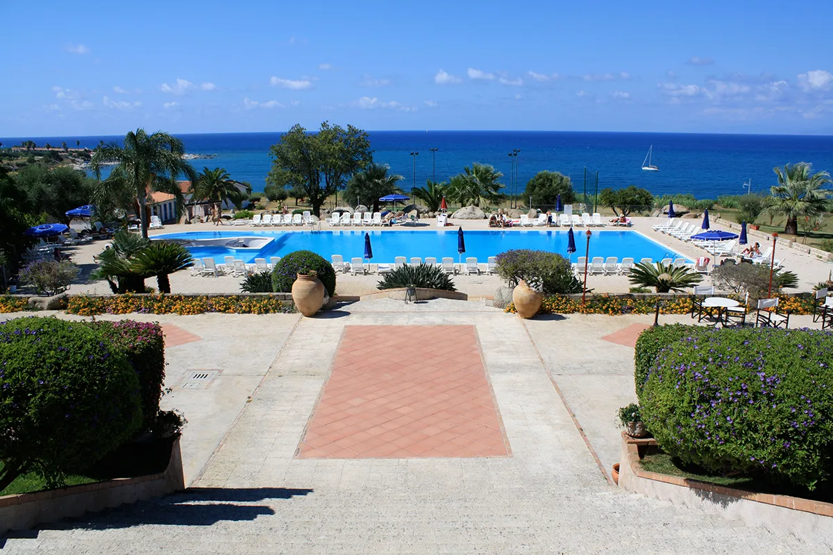 Piscina del resort vista dalla terrazza con giardino fiorito e mare sullo sfondo