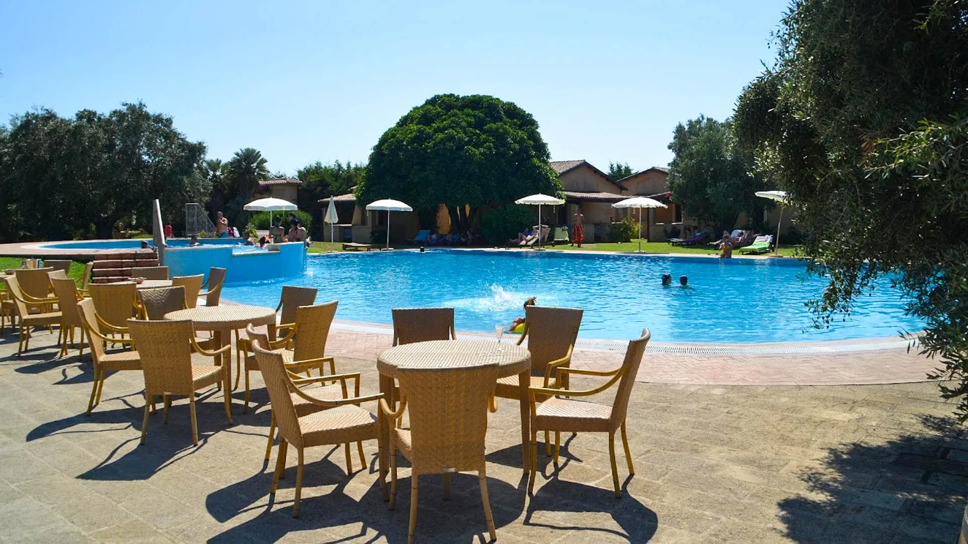 Area relax a bordo piscina con tavoli e sedie in vimini e ospiti in acqua