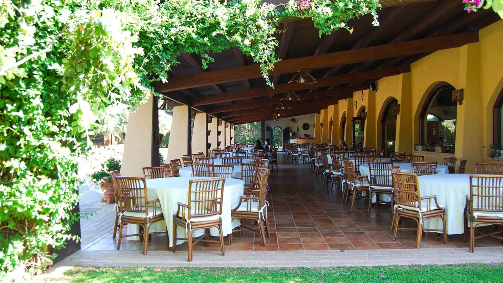 Terrazza ristorante coperta con tavoli rotondi, sedie in legno e bouganville