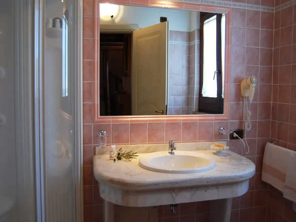 Bagno con piastrelle rosa, lavabo in marmo, specchio grande e doccia