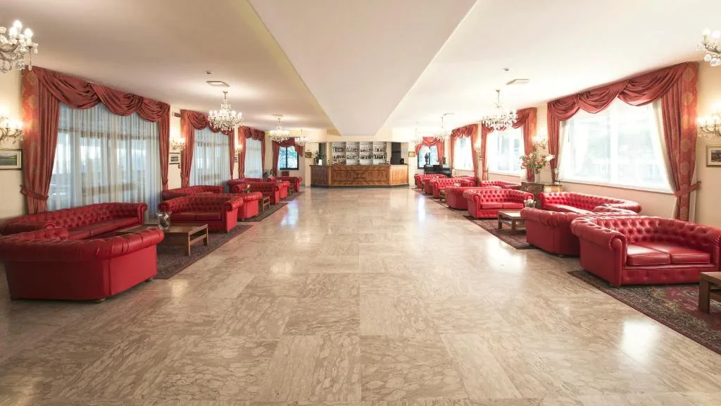 Ampia hall dell'hotel con divani in pelle rossa capitonné, lampadari e pavimento in marmo