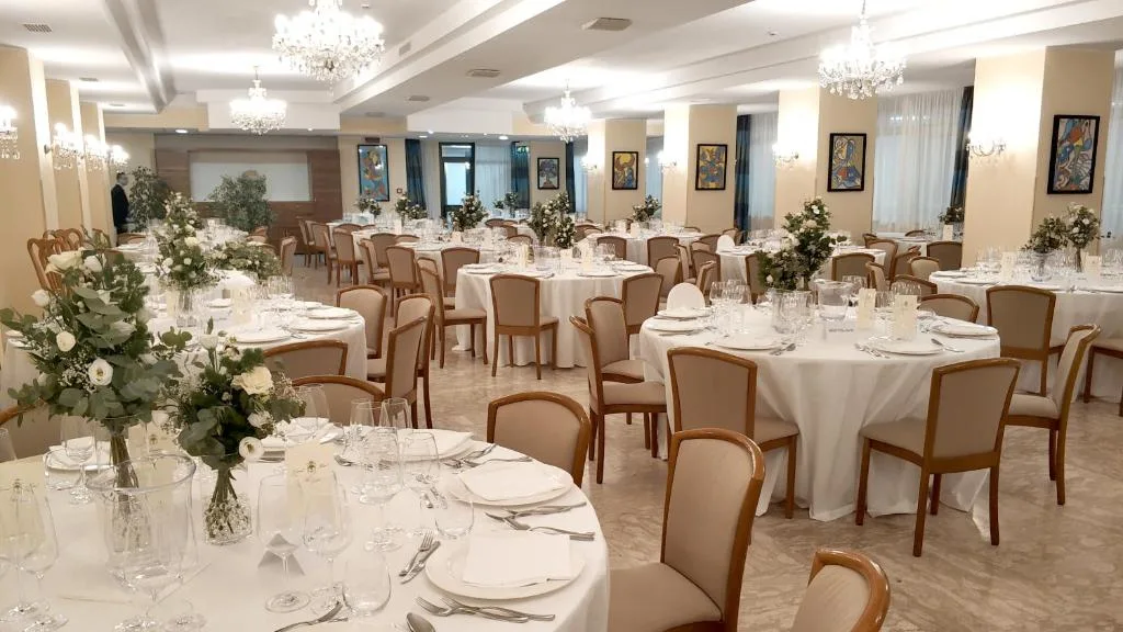 Sala ristorante elegante allestita per banchetto con tavoli rotondi e centrotavola floreali