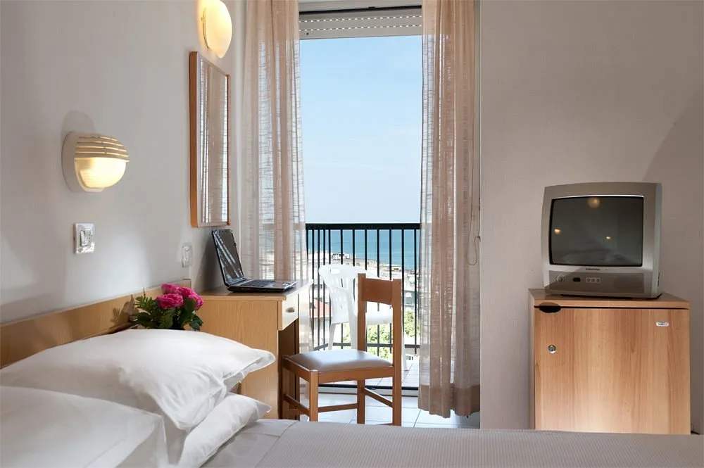 Camera con letto, scrivania con laptop, TV e balcone affacciato sul mare