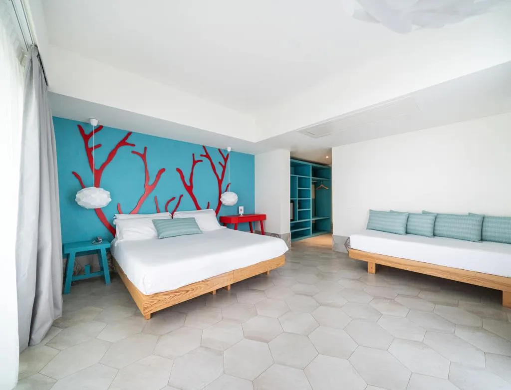 Camera spaziosa con parete azzurra decorata a coralli rossi, letto matrimoniale e divano