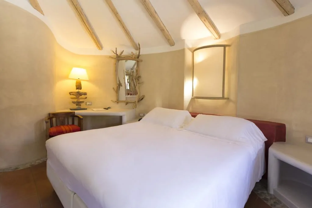 Camera rustica con soffitto a travi, letto matrimoniale bianco e arredi in stile mediterraneo