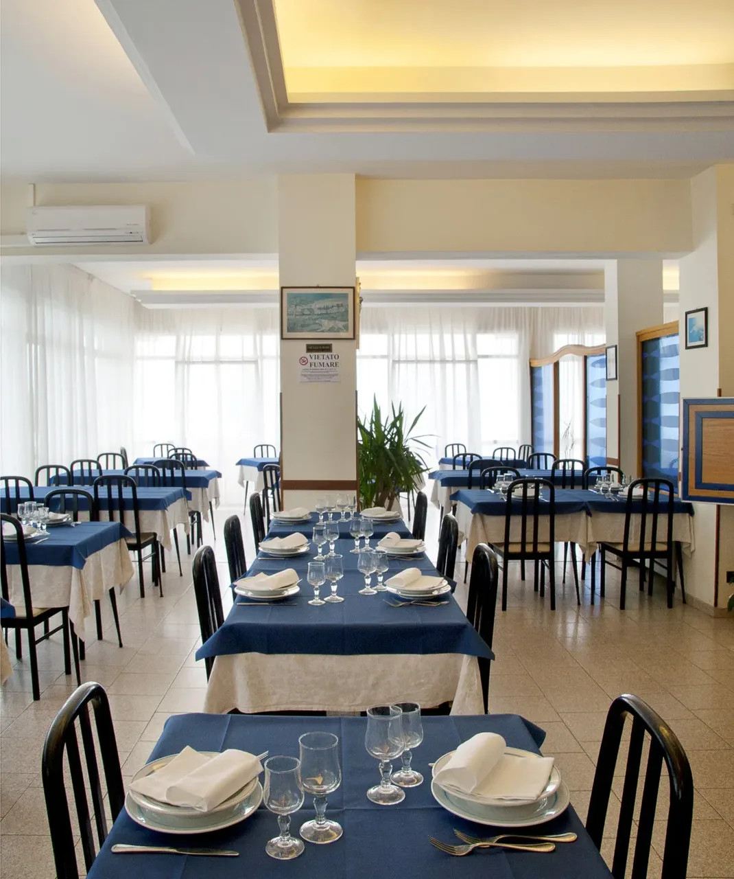 Sala da pranzo luminosa con tavoli blu apparecchiati e sedie nere