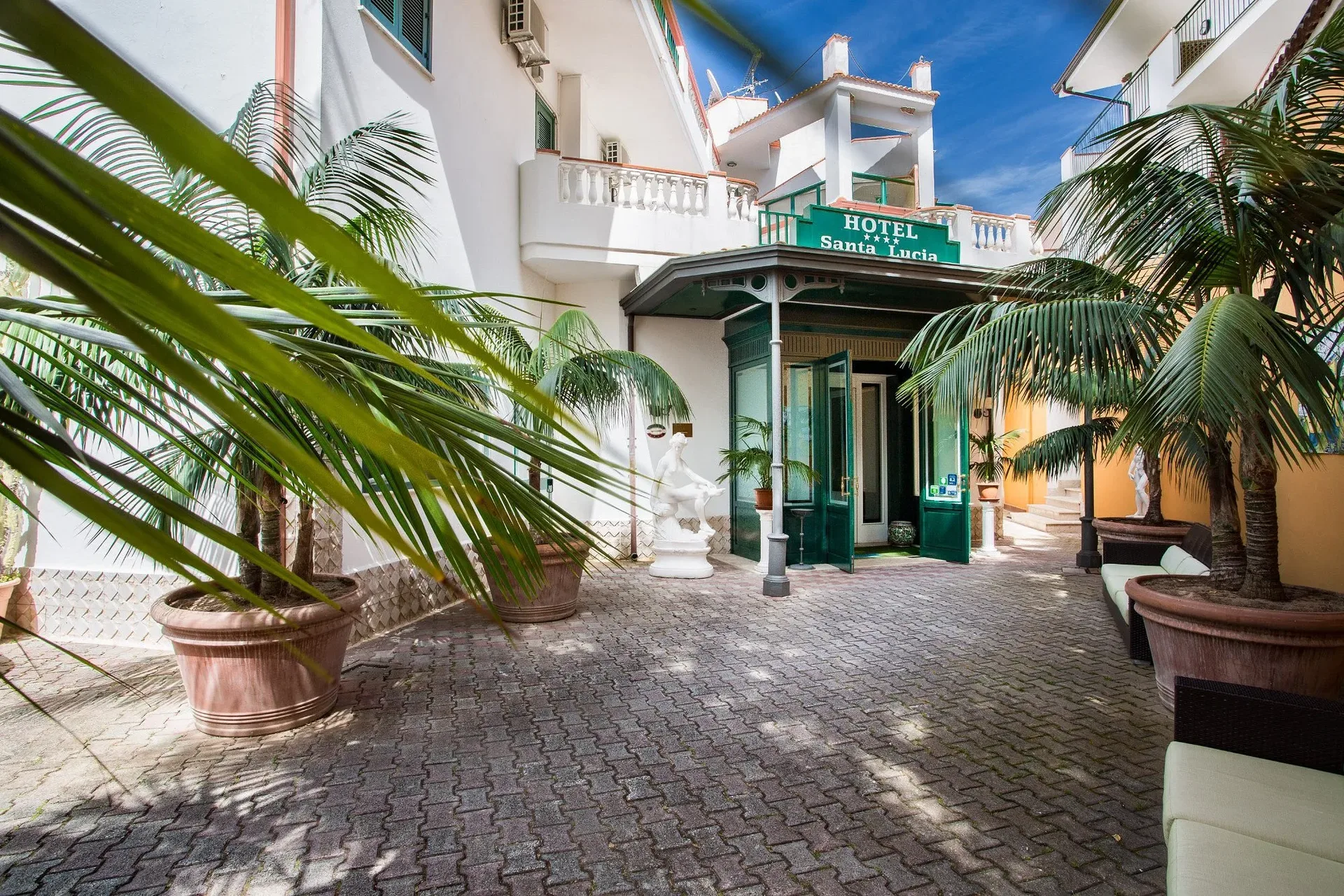 Ingresso dell'hotel Santa Lucia con palme in vaso e statue decorative