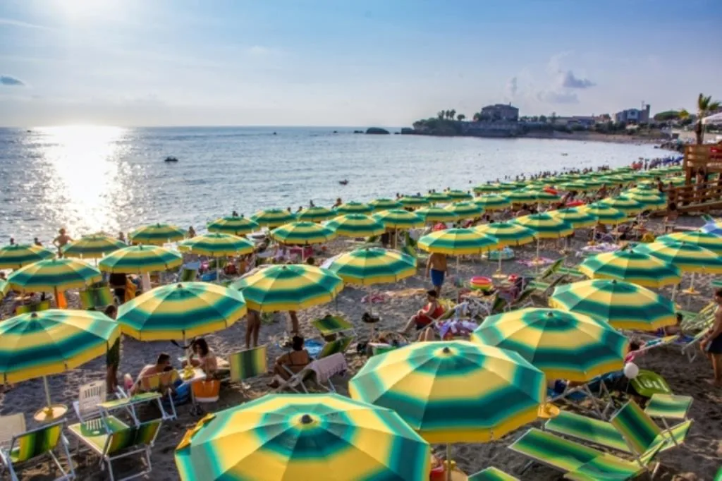 Spiaggia affollata con ombrelloni gialli e verdi e vista sul mare al tramonto