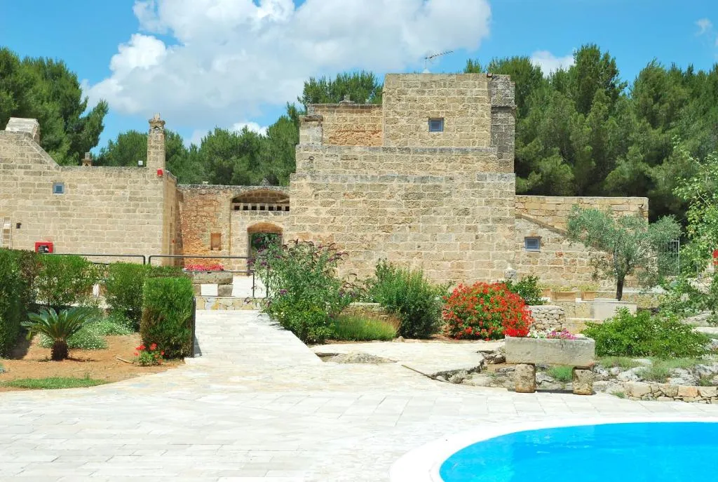 Masseria in pietra con torre, giardino fiorito e bordo piscina