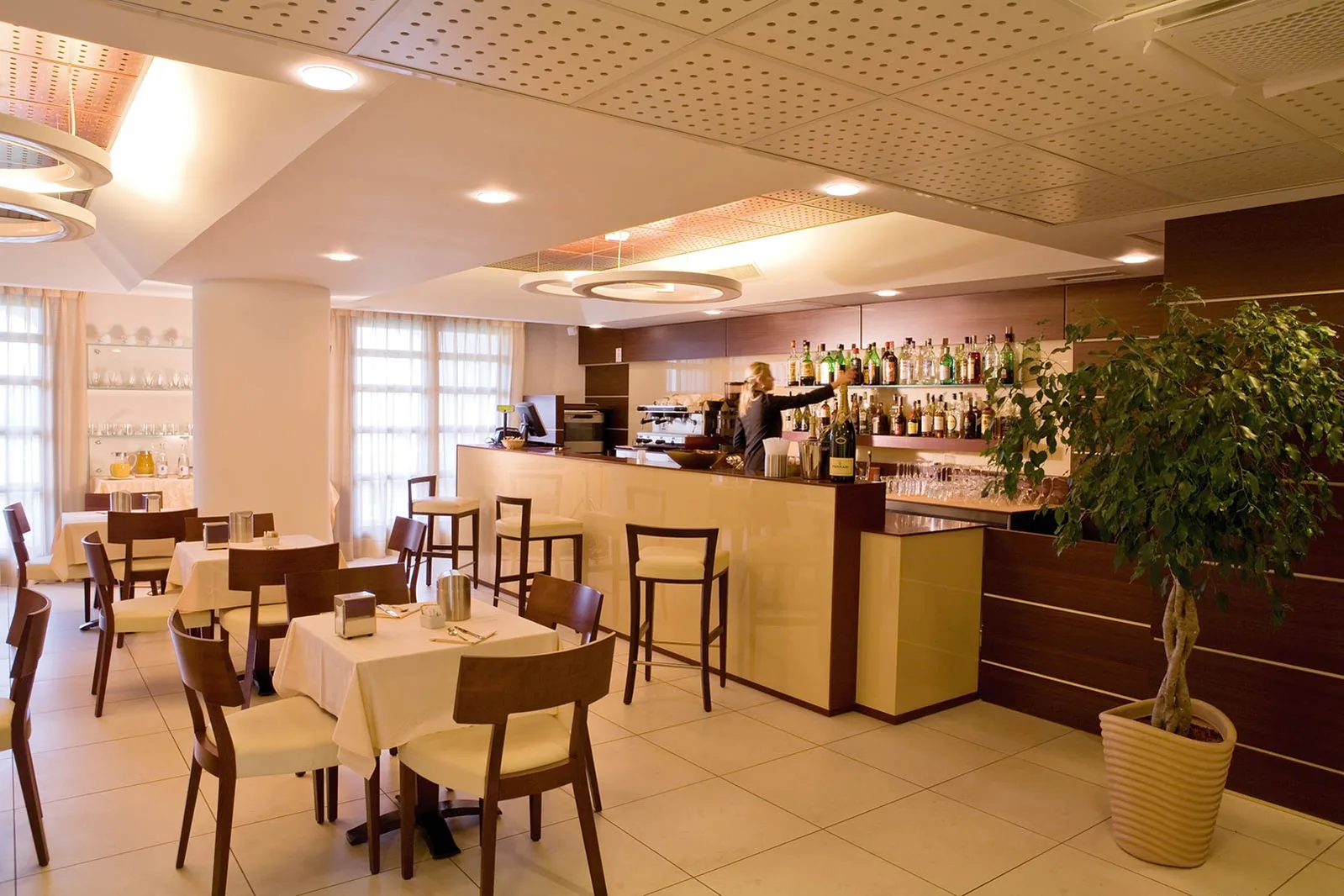 Interno del bar ristorante con tavoli apparecchiati, sedie in legno e bancone con bottiglie