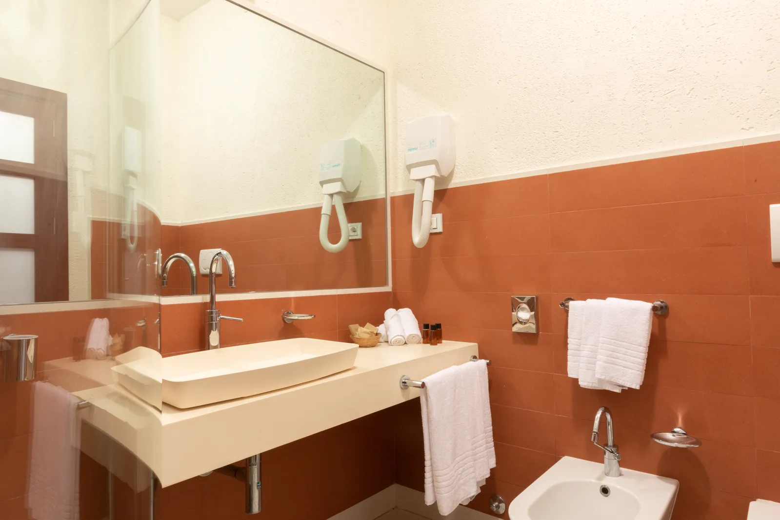 Bagno moderno con lavabo da appoggio, grande specchio, asciugacapelli e pareti color terracotta