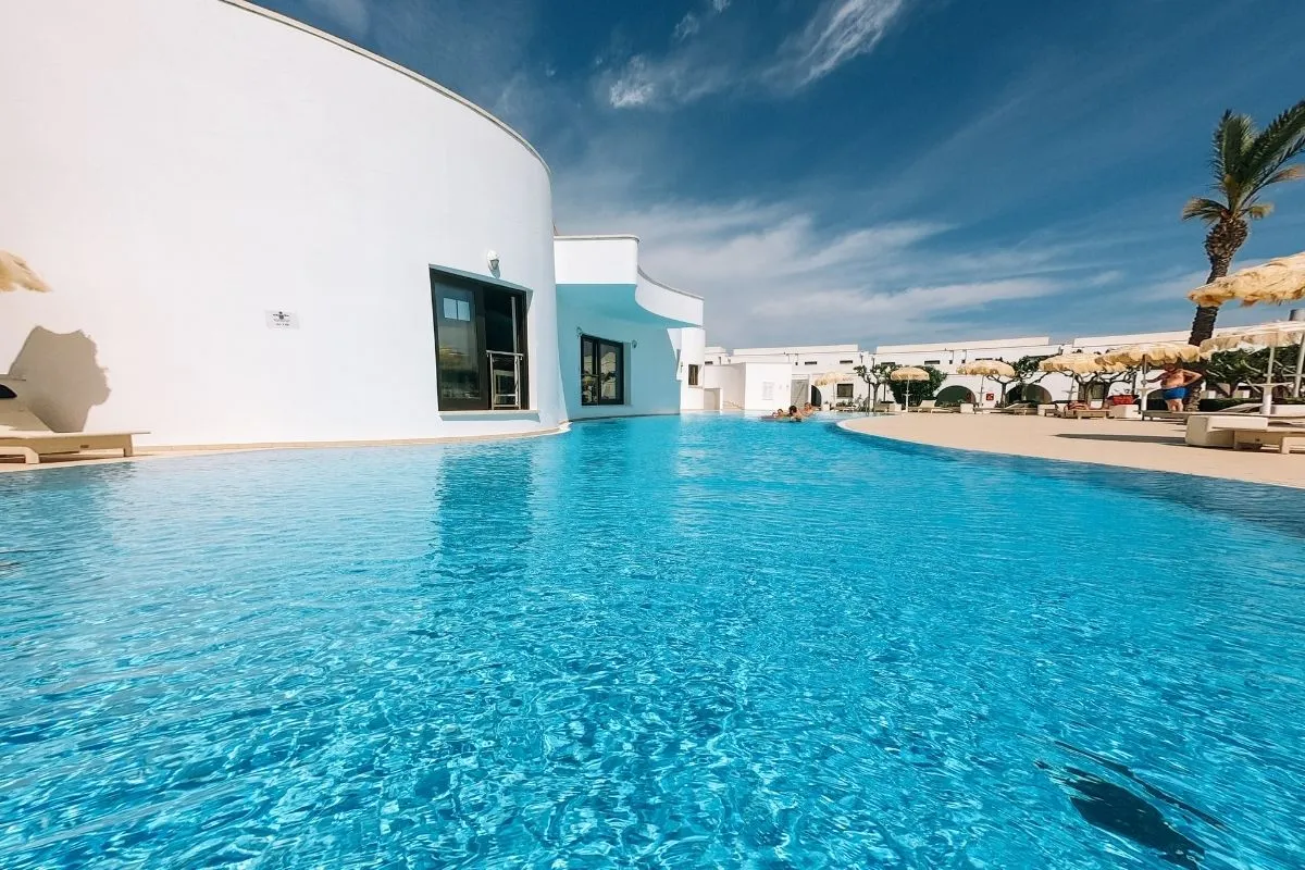 Piscina dall'acqua turchese accanto a edificio bianco con palma e cielo azzurro