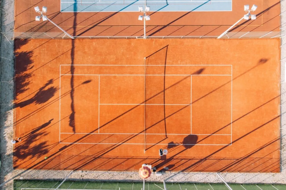 Veduta aerea del campo da tennis in terra rossa con ombre delle palme