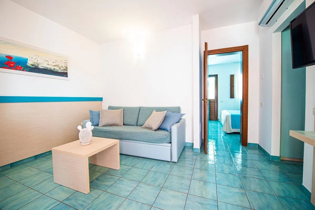 Soggiorno della suite con divano azzurro e camera da letto sul fondo