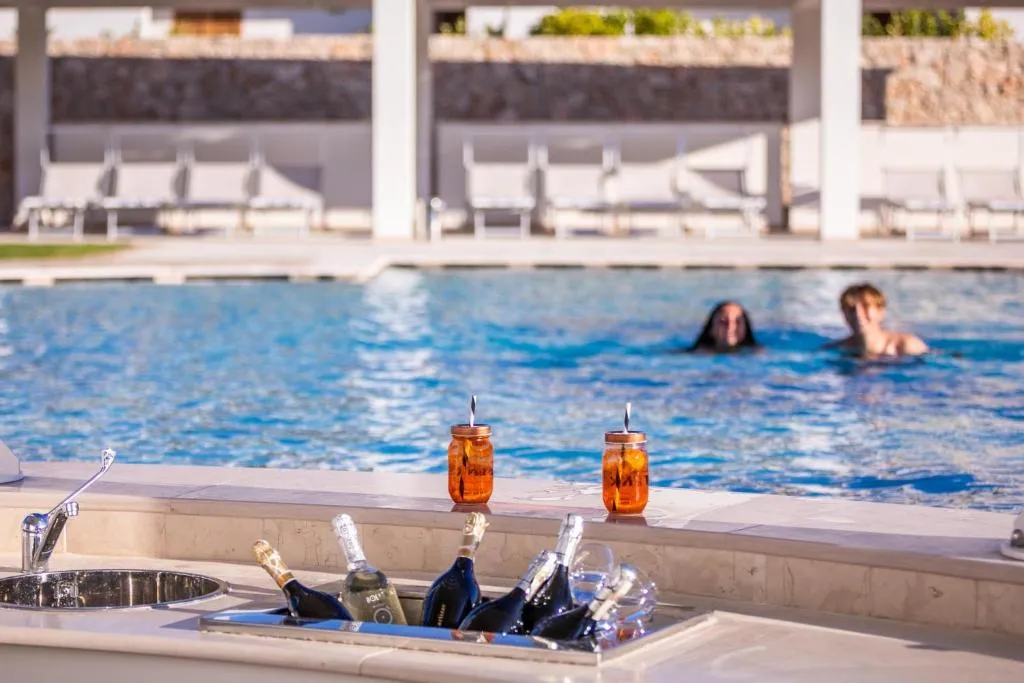 Bottiglie di spumante e cocktail al bordo piscina con ospiti in acqua