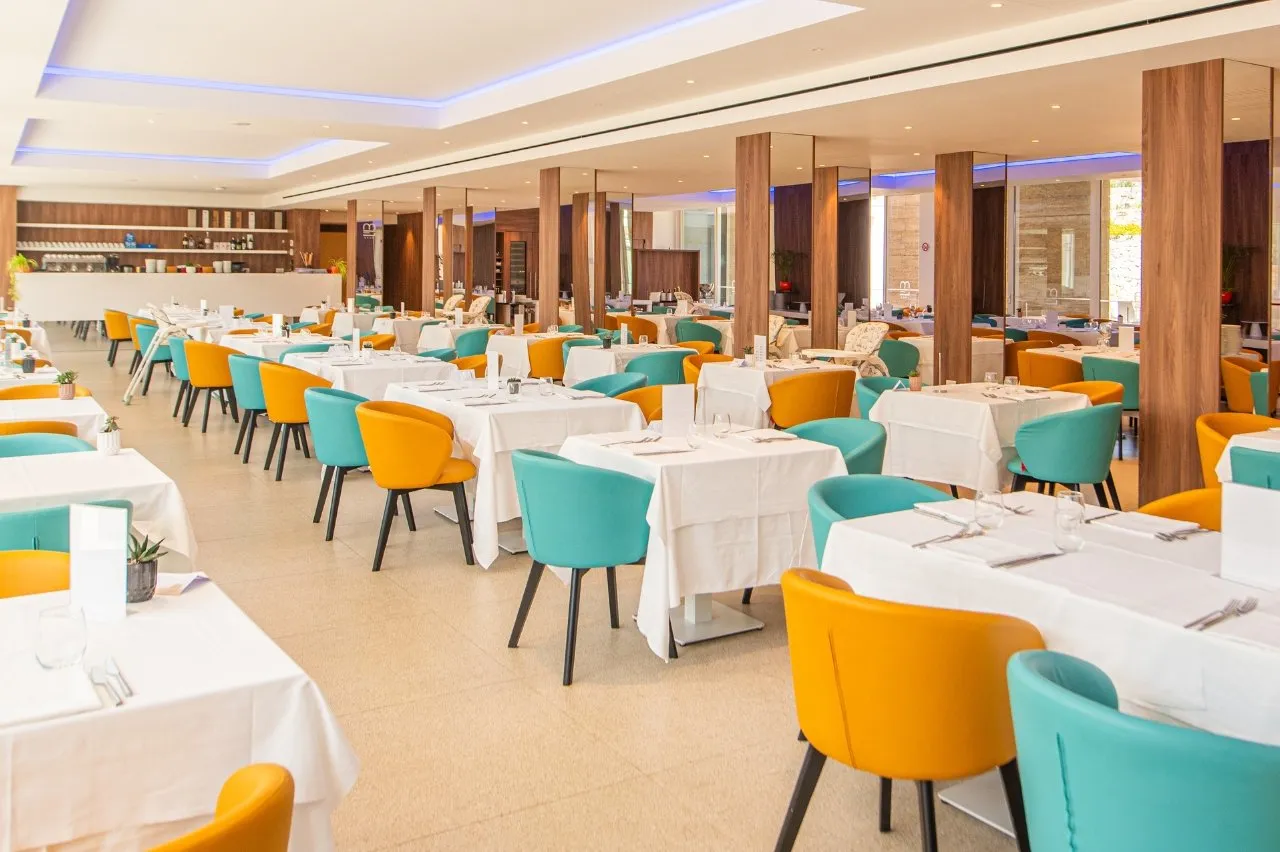 Sala ristorante con tavoli apparecchiati e sedie color turchese e arancione