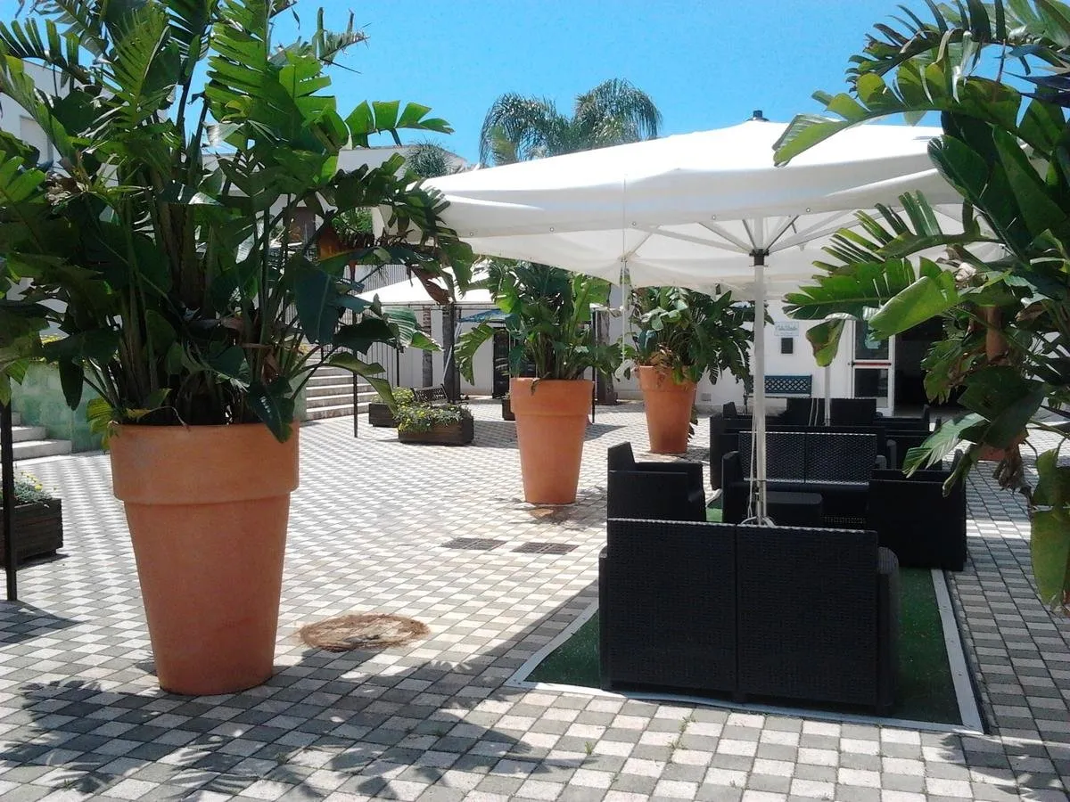 Zona relax all'aperto con ombrellone bianco, divani e piante tropicali