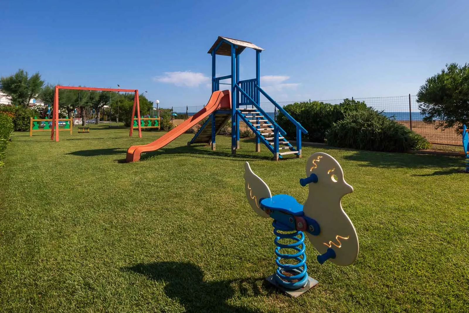 Parco giochi per bambini con scivolo, altalena e giochi a molla nel prato verde con vista mare