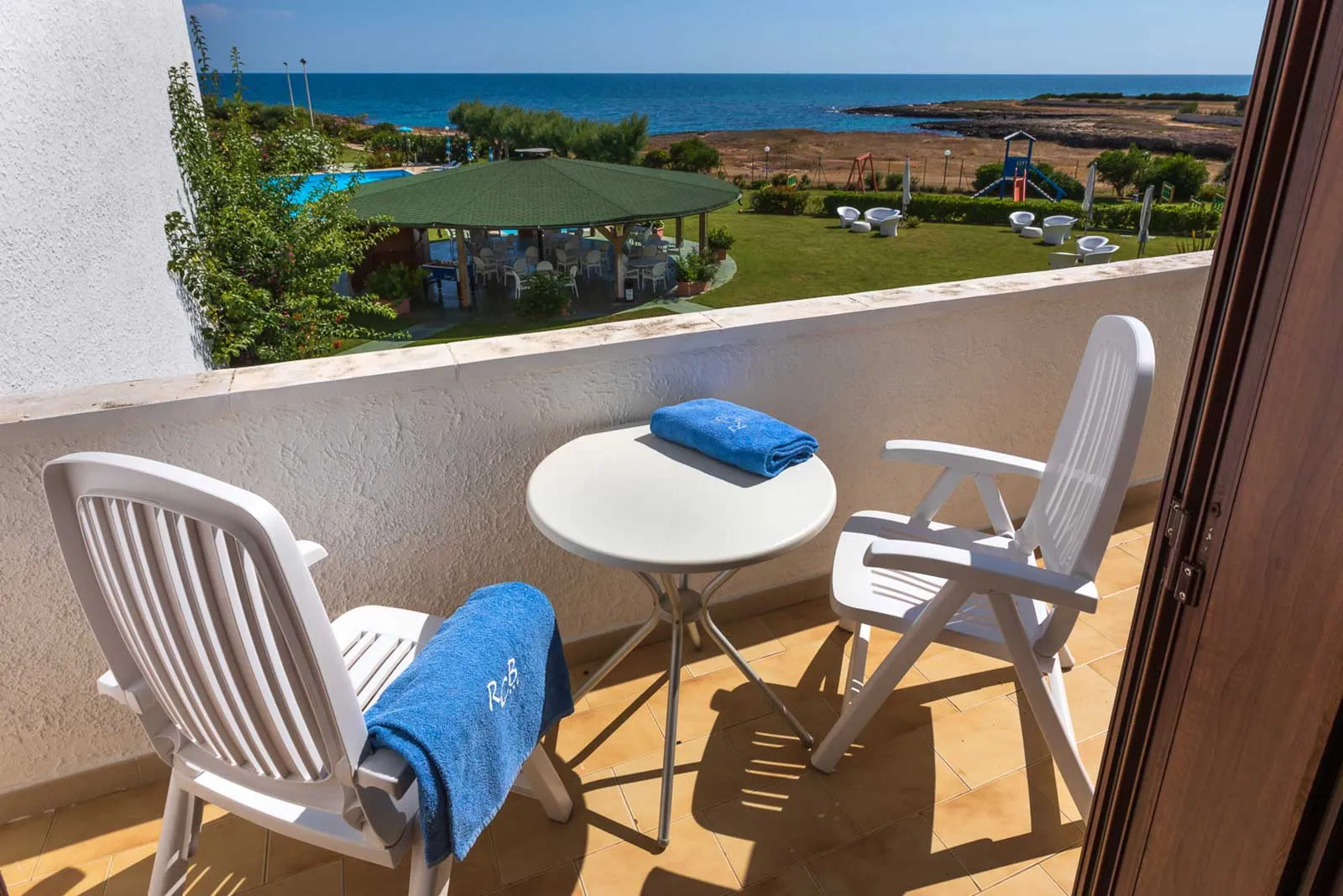 Balcone con tavolo e sedie bianche affacciato sulle piscine, gazebo e mare