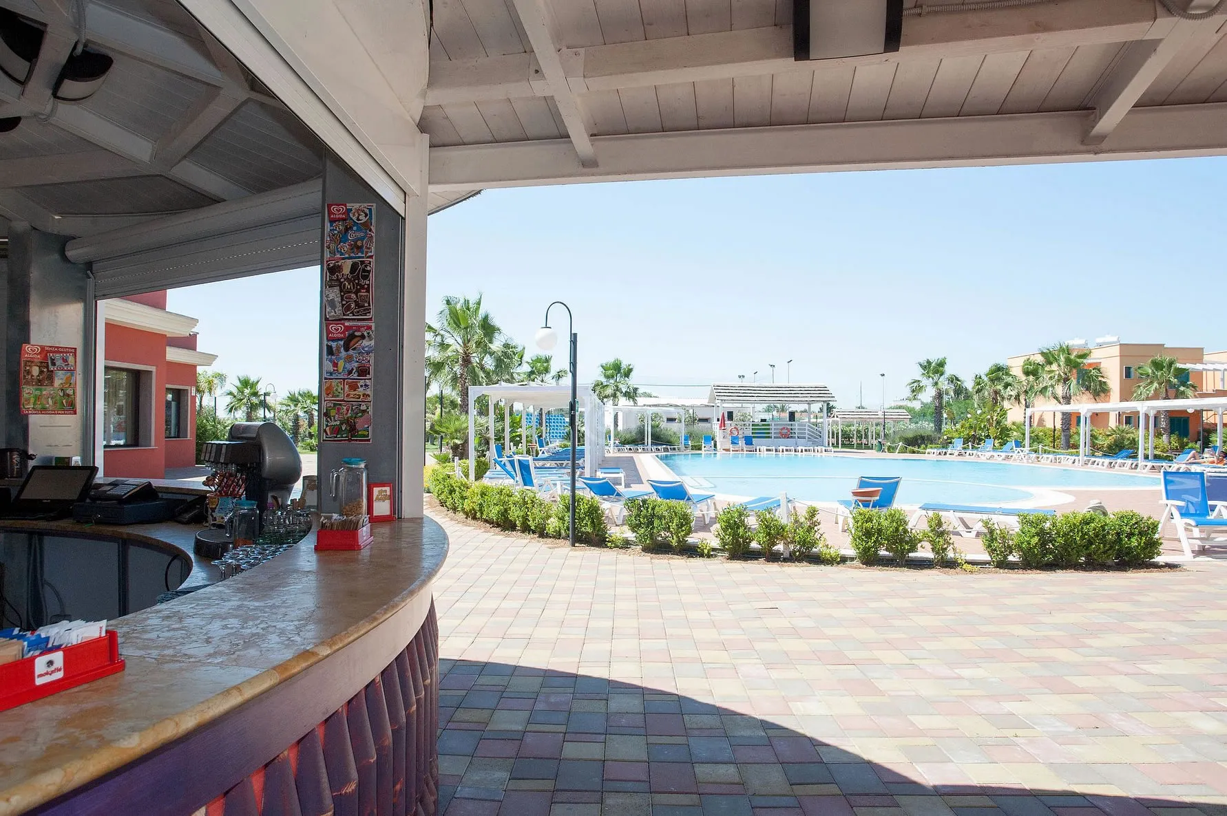 Bar a bordo piscina con bancone e vista sulla piscina e palme del resort