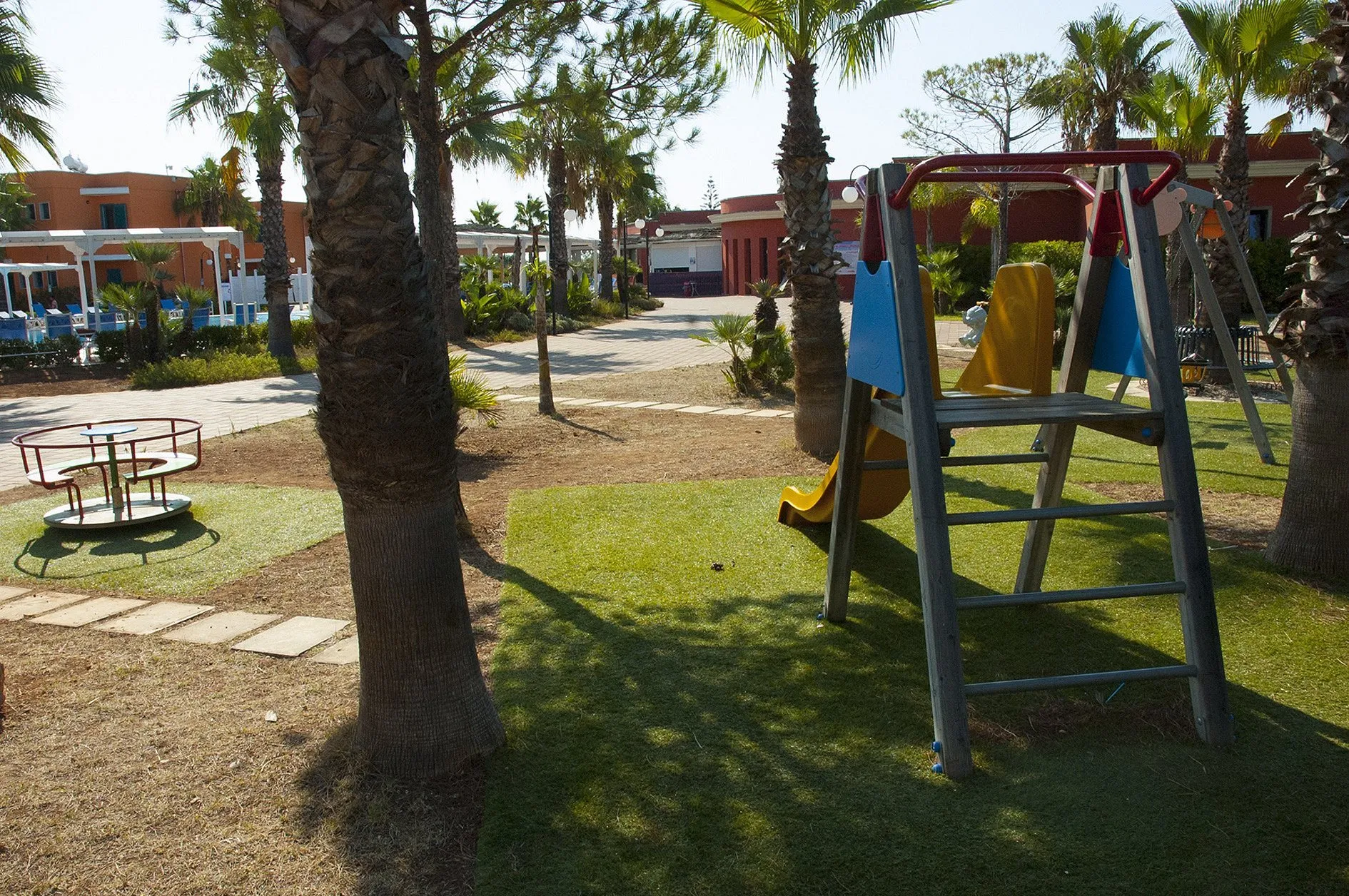 Area giochi per bambini con scivolo e giostrina tra le palme nel giardino del resort