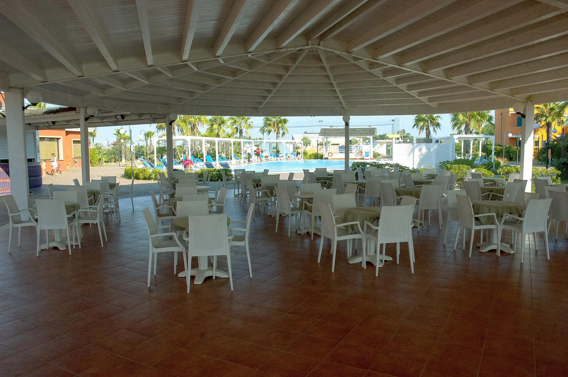 Ampia area ristorante coperta con tavoli e sedie bianche affacciata sulla piscina