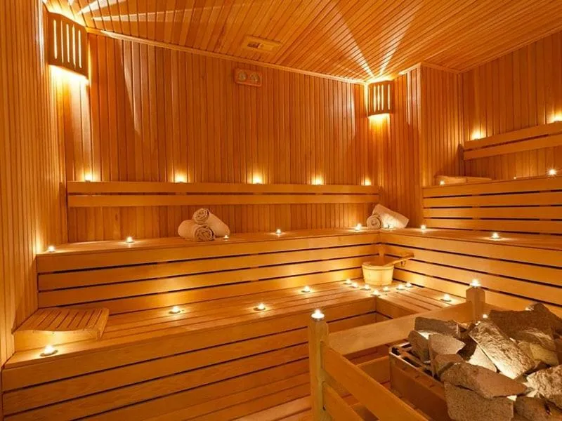 Sauna in legno illuminata da candele con asciugamani arrotolati e stufa con pietre