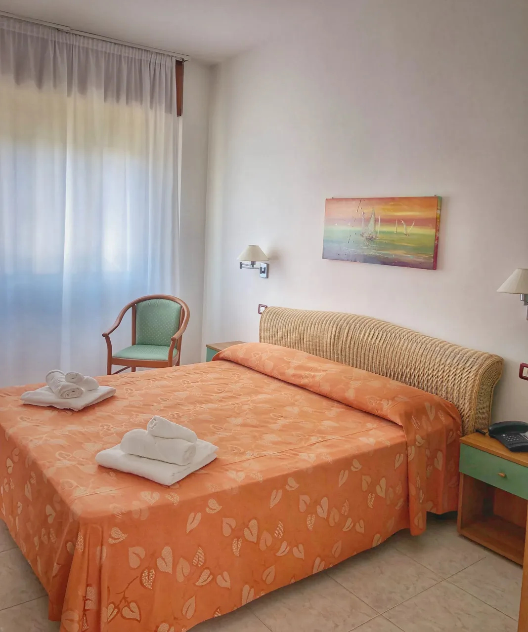 Camera luminosa con letto matrimoniale arancione, testiera in vimini e poltrona verde