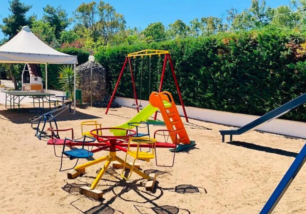 Area giochi per bambini con giostra, scivolo e altalena su sabbia