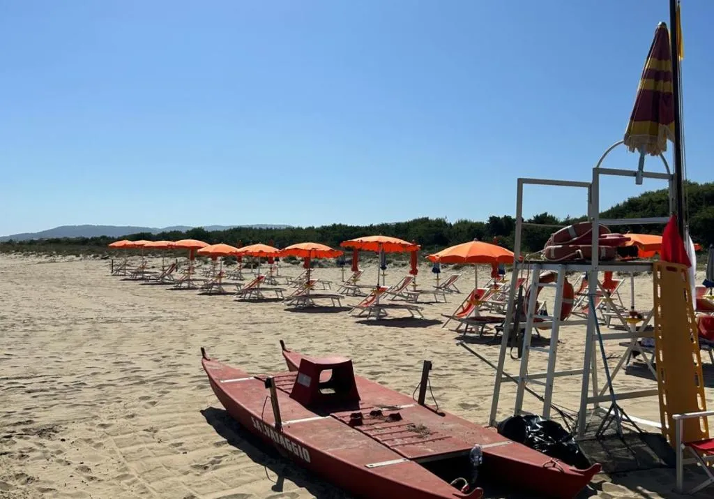 Spiaggia con ombrelloni arancioni, lettini, pattino di salvataggio e torretta