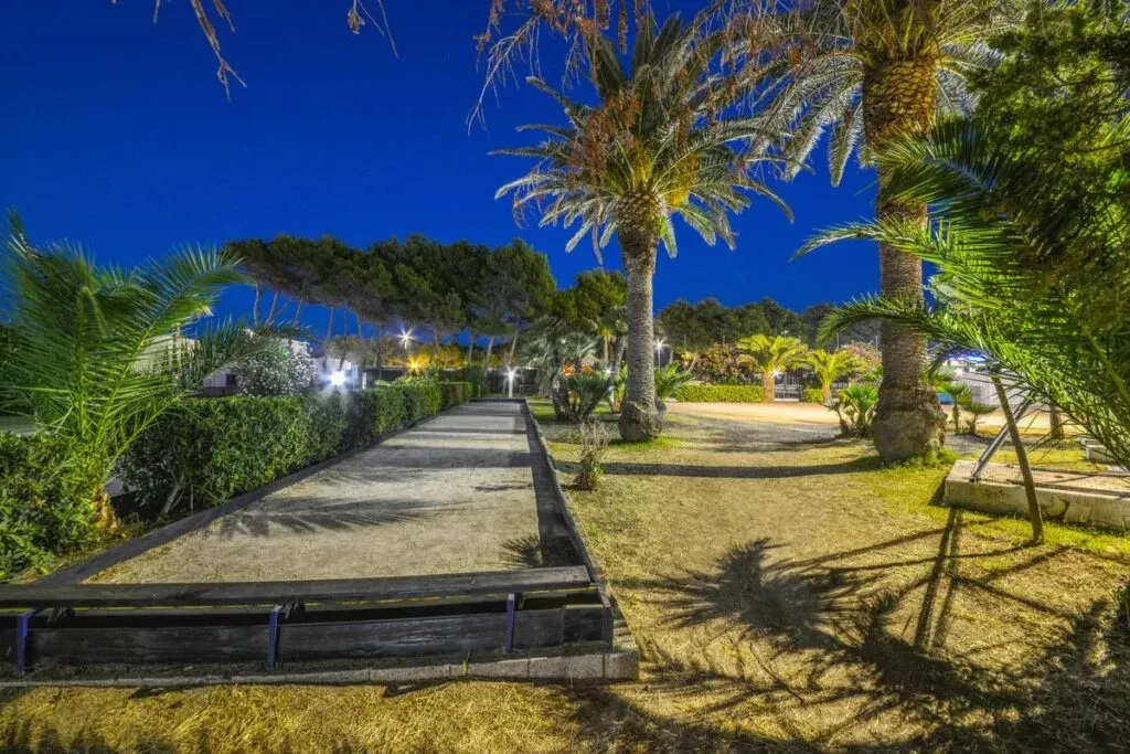 Campo da bocce e giardino con palme illuminato di sera