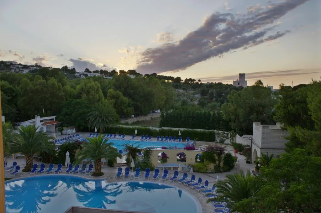 Vista dall'alto delle piscine dell'hotel al tramonto circondate da palme e vegetazione
