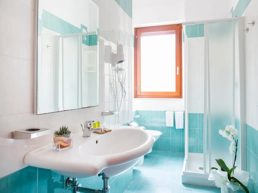 Bagno con piastrelle azzurre, lavabo, doccia e finestra