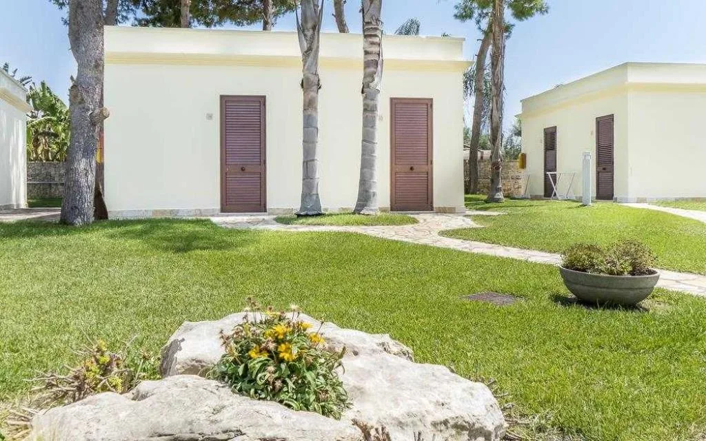 Bungalow bianchi con porte in legno scuro immersi nel giardino con palme e prato