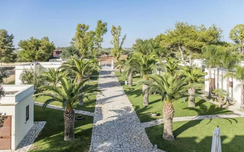 Giardino con vialetto in pietra, palme e prato verde tra i bungalow